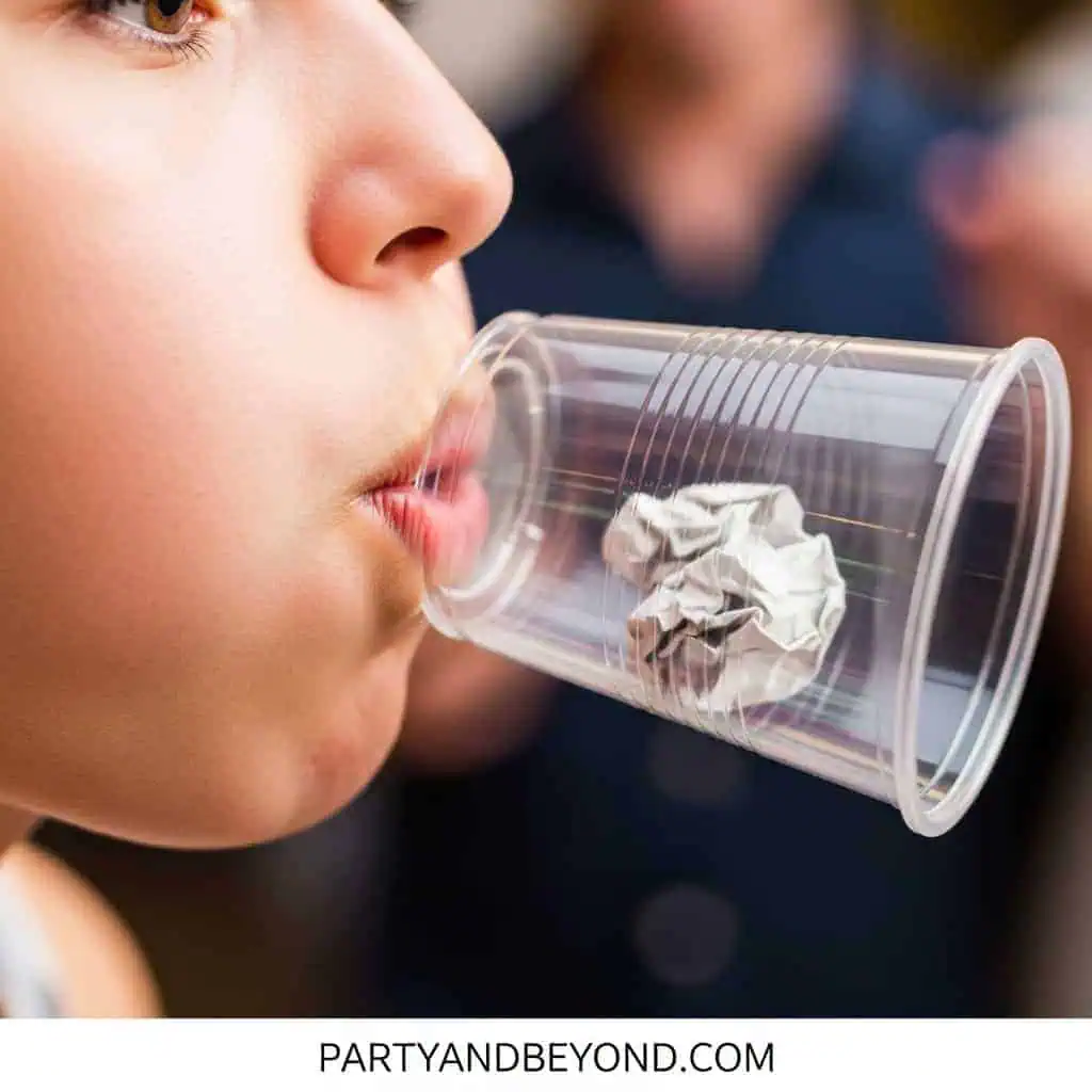 Child blowing into a plastic cup with crumpled paper for a party game.
