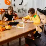 25 Best Halloween Games for Kids – Fun, Spooky & Easy to Play! Kids making Halloween crafts at a themed party with pumpkins and decorations.