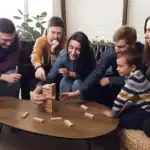 31 Cool Minute to Win It Party Games for Adults Group of adults and a child playing Jenga at a cozy indoor gathering.