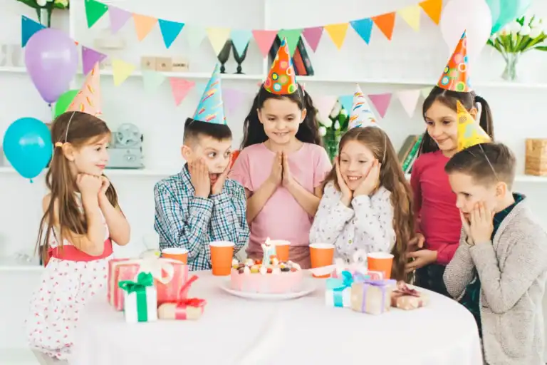 Kids celebrating birthday with party hats, cake, and gifts at a fun party.
