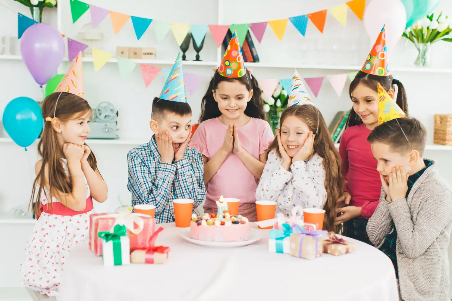 Kids celebrating birthday with party hats, cake, and gifts at a fun party.