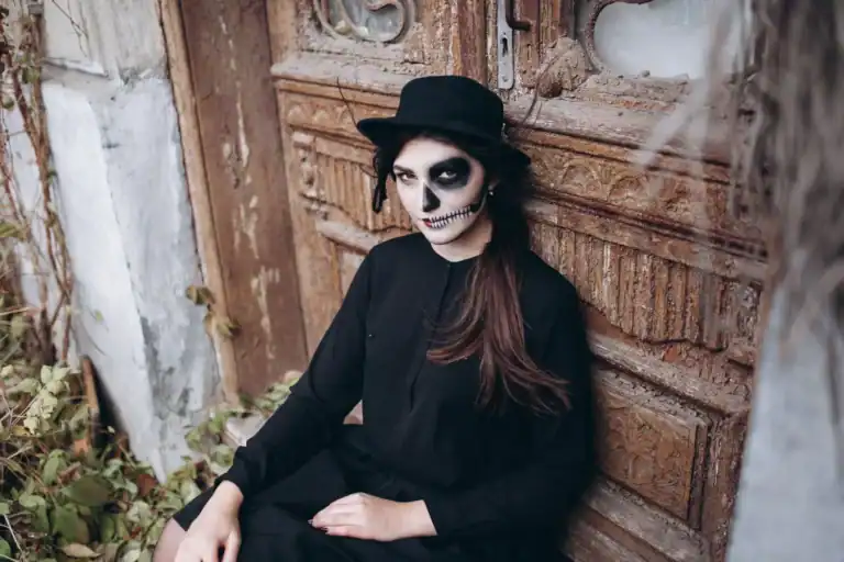 Woman with skull makeup, black hat, and dark outfit for Halloween costume.