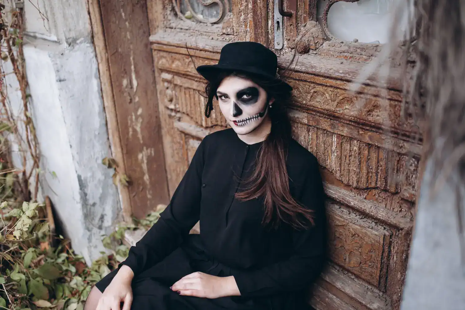 Woman with skull makeup, black hat, and dark outfit for Halloween costume.