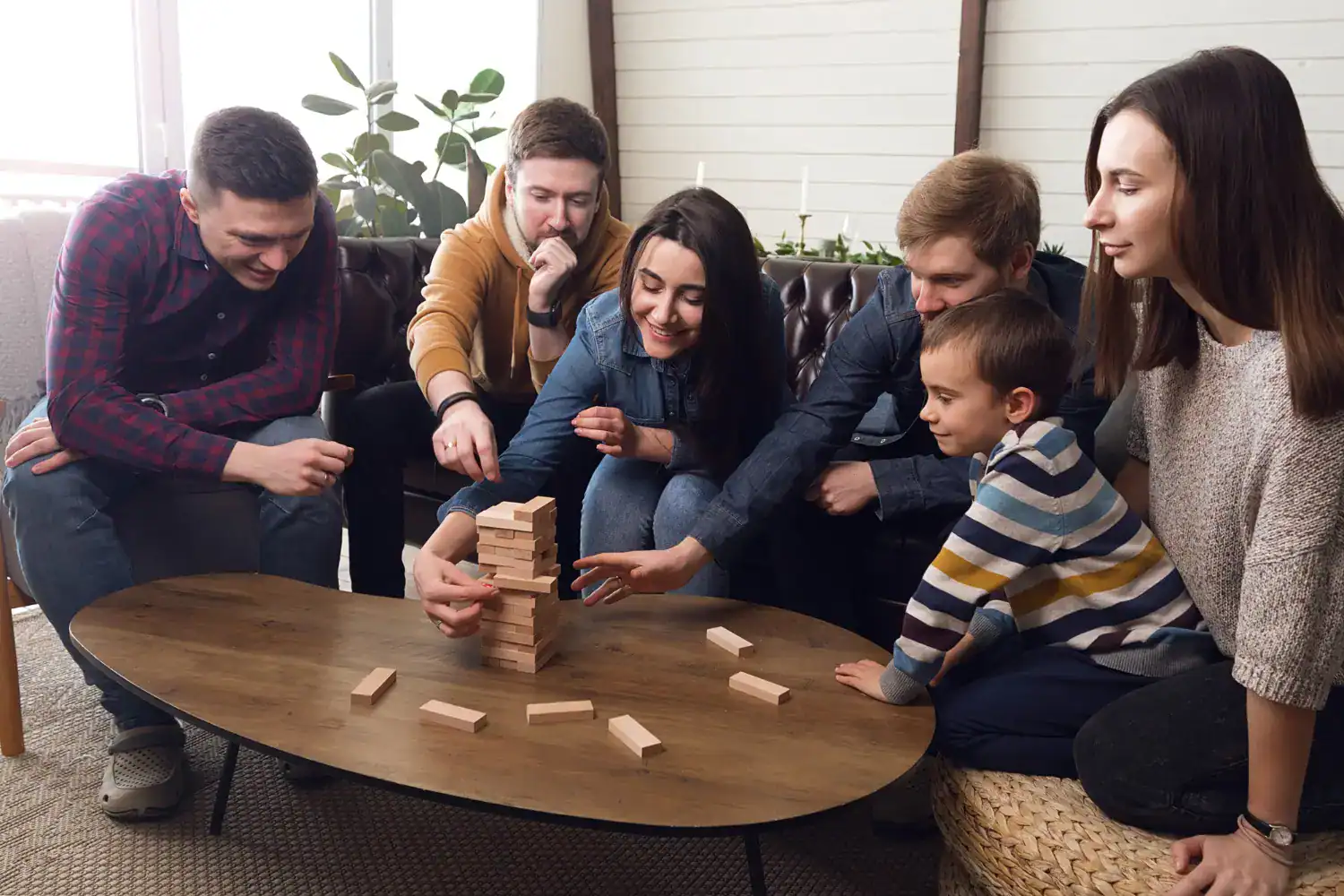 Group of adults and a child playing Jenga at a cozy indoor gathering.