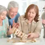 17 Unique Party Games for Senior Citizens Celebrations Senior citizens enjoying a lively game of giant Jenga at a celebration.