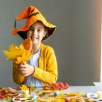 29 Easy And Engaging Fall Craft Ideas for Kids Happy girl in fall costume with leaves, celebrating autumn crafts for kids.