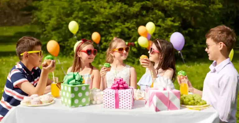 Kids enjoying birthday party with colorful balloons and treats outdoors.