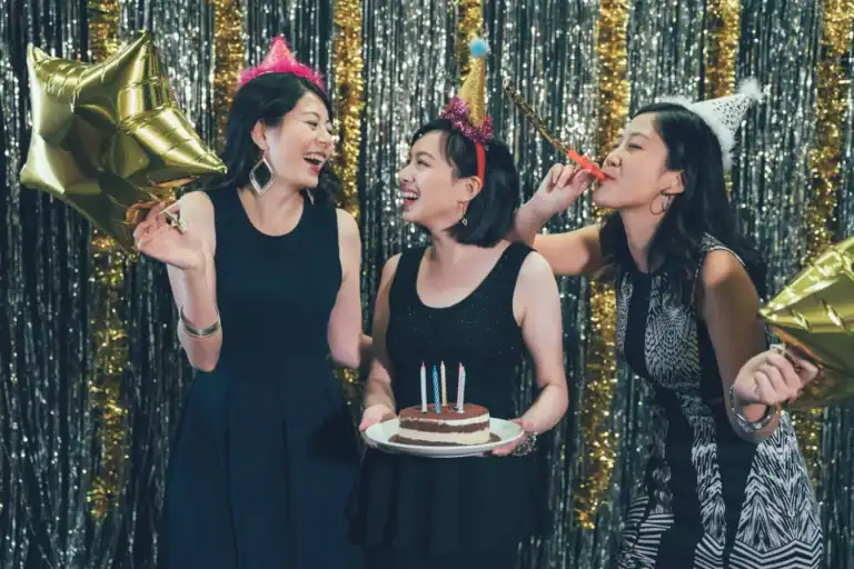 Young women celebrating a Sweet 16 birthday with party hats, balloons, and cake at a festive event.