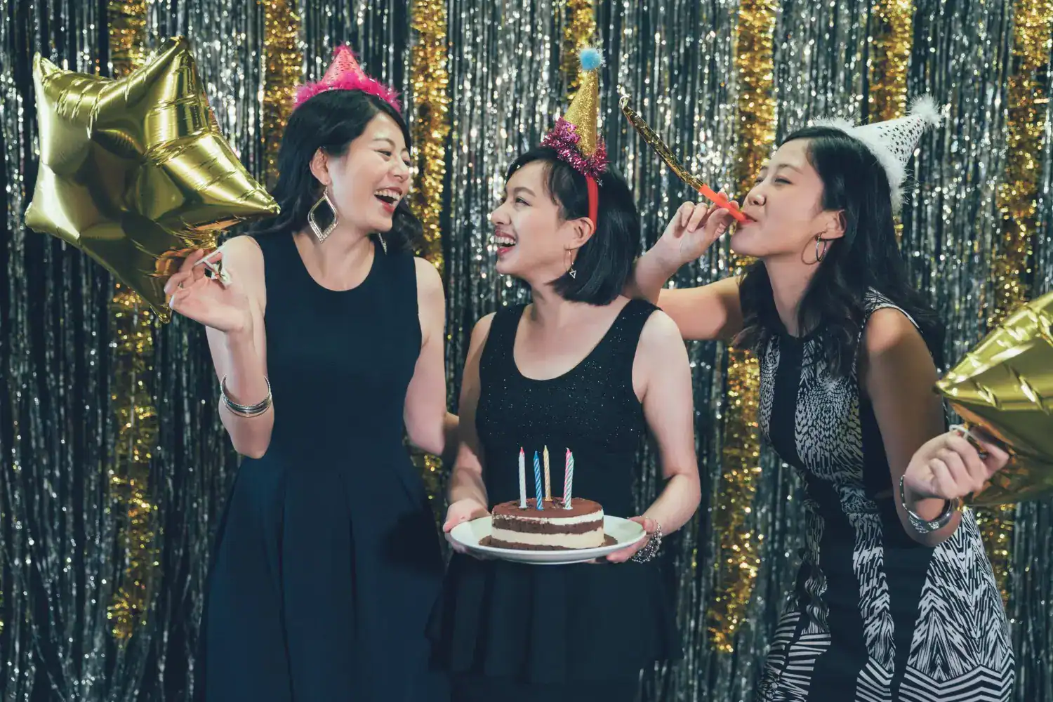 Young women celebrating a Sweet 16 birthday with party hats, balloons, and cake at a festive event.