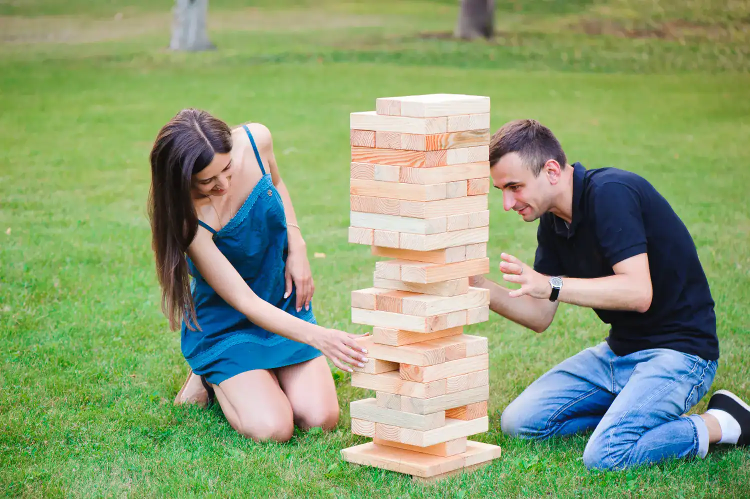 Engaged couple playing giant Jenga game outdoors at wedding reception.
