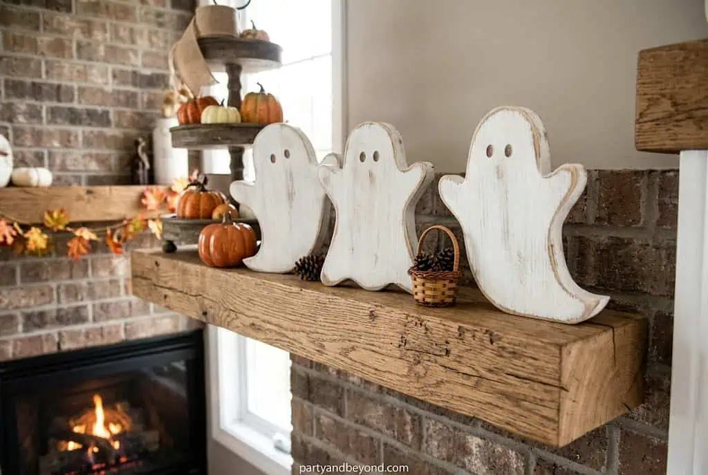 three white ghost wood cutouts displayed together on a Halloween mantel