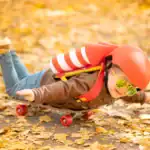 21 Festive Fall Party Games for Kids’ Seasonal Fun Child in helmet and goggles skateboarding on autumn leaves trail.