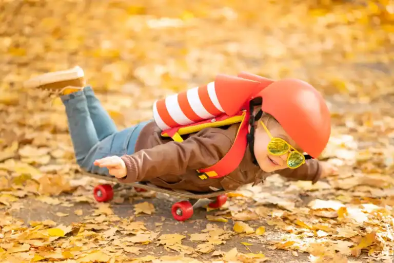 Child in helmet and goggles skateboarding on autumn leaves trail.
