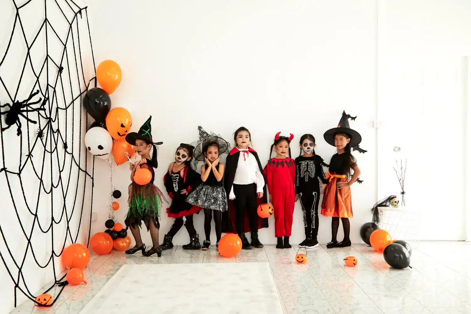 Kids dressed in Halloween costumes with pumpkins and decorations for spooky party.