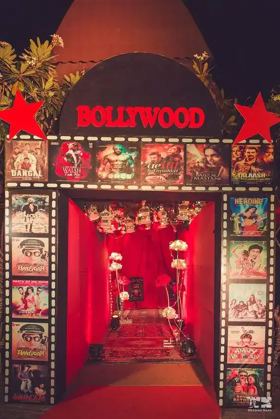 Bollywood-themed wedding reception entrance with vibrant red and black colors, film posters, and dec.