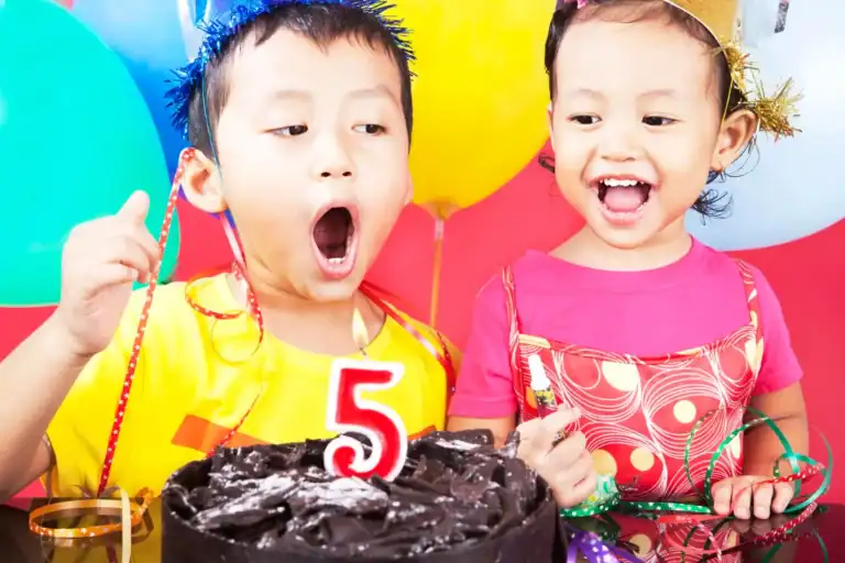 Happy children celebrating 5th birthday with cake and balloons.