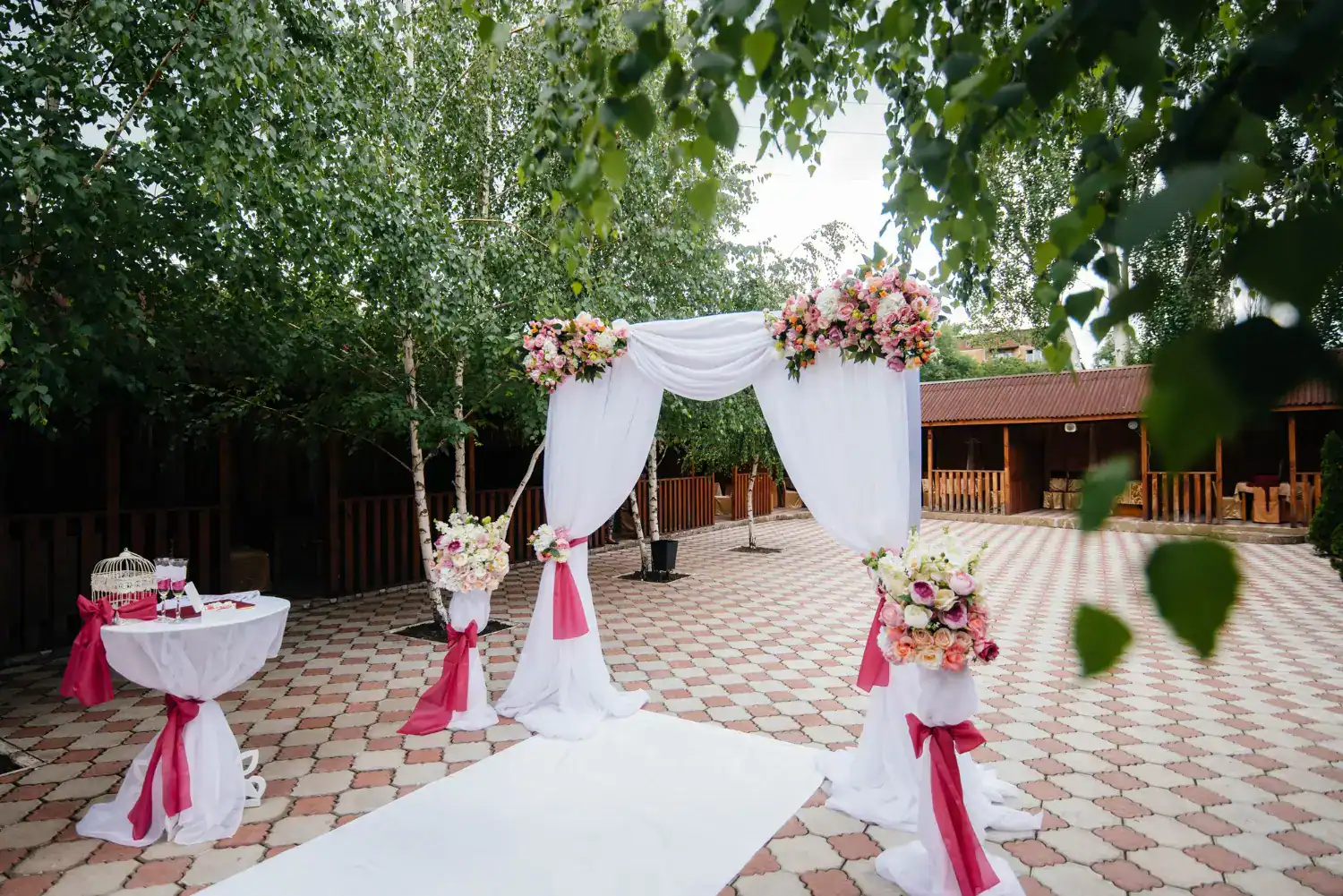 Outdoor wedding entrance with floral arrangements and white drapery.