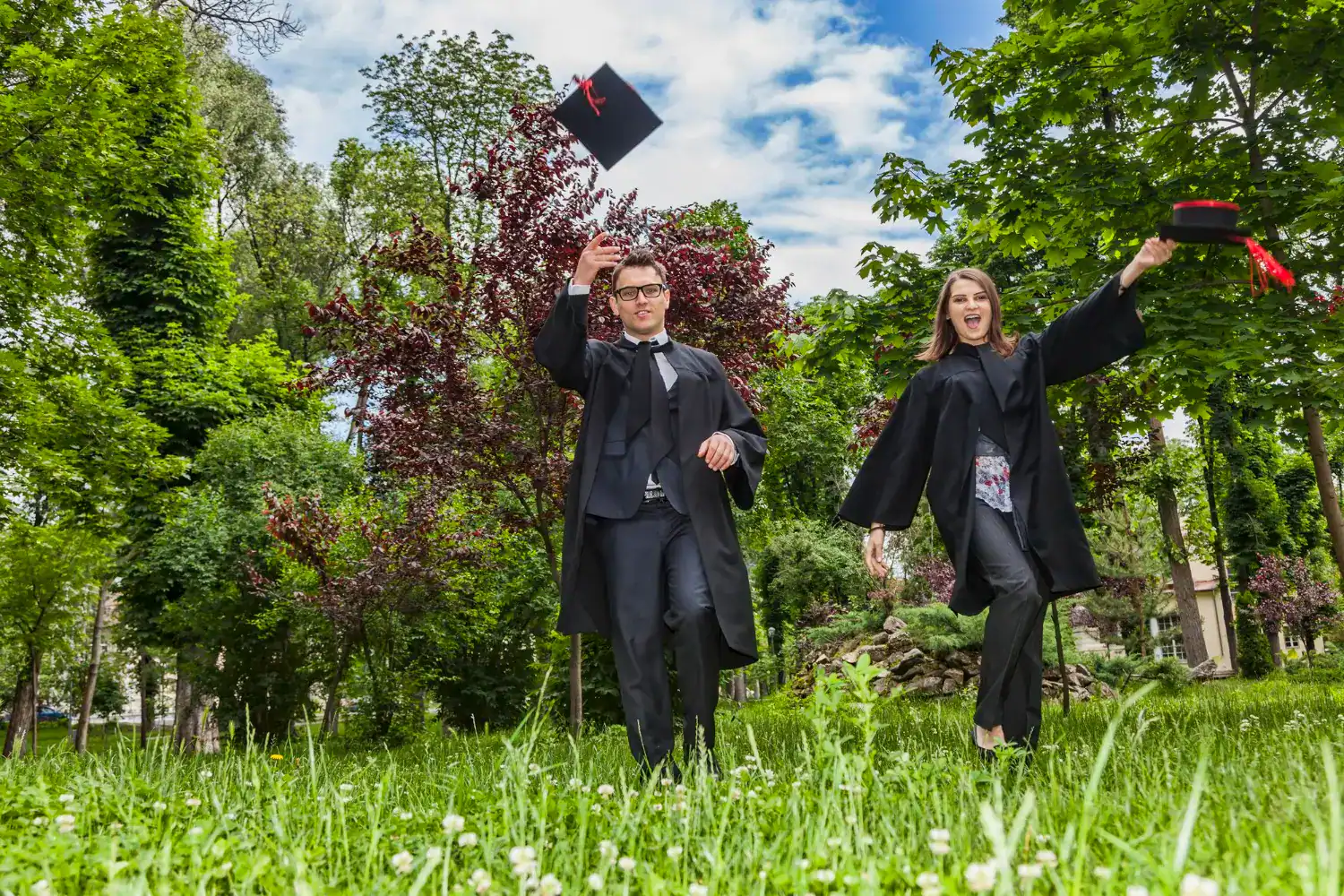 Graduates in caps and gowns celebrating outdoors in a lush green park.