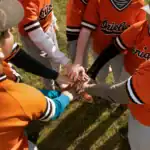 26 Electrifying Football Game Themes to Supercharge Your Event Kids in orange baseball uniforms huddling with hands together on the field.