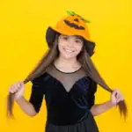 21 Teen Girl Halloween Costume Ideas That Are Actually Cool in 2026 Cute girl in a pumpkin-themed Halloween costume with a pumpkin hat.