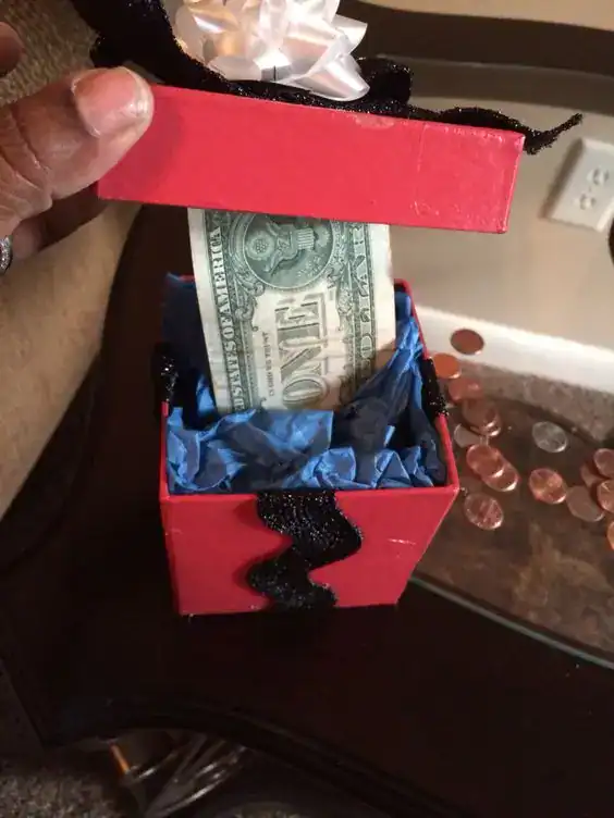 Deep gift box with tissue paper layers hiding dollar bills throughout, a surprise money gift for teens