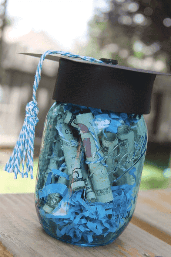 Graduation cap-shaped jar filled with rolled dollar bills and shredded paper, perfect for celebratin.