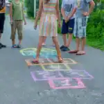 21 Simple Group Games for Kids to Play Anytime, Anywhere Kids playing hopscotch outdoors on a sunny day.