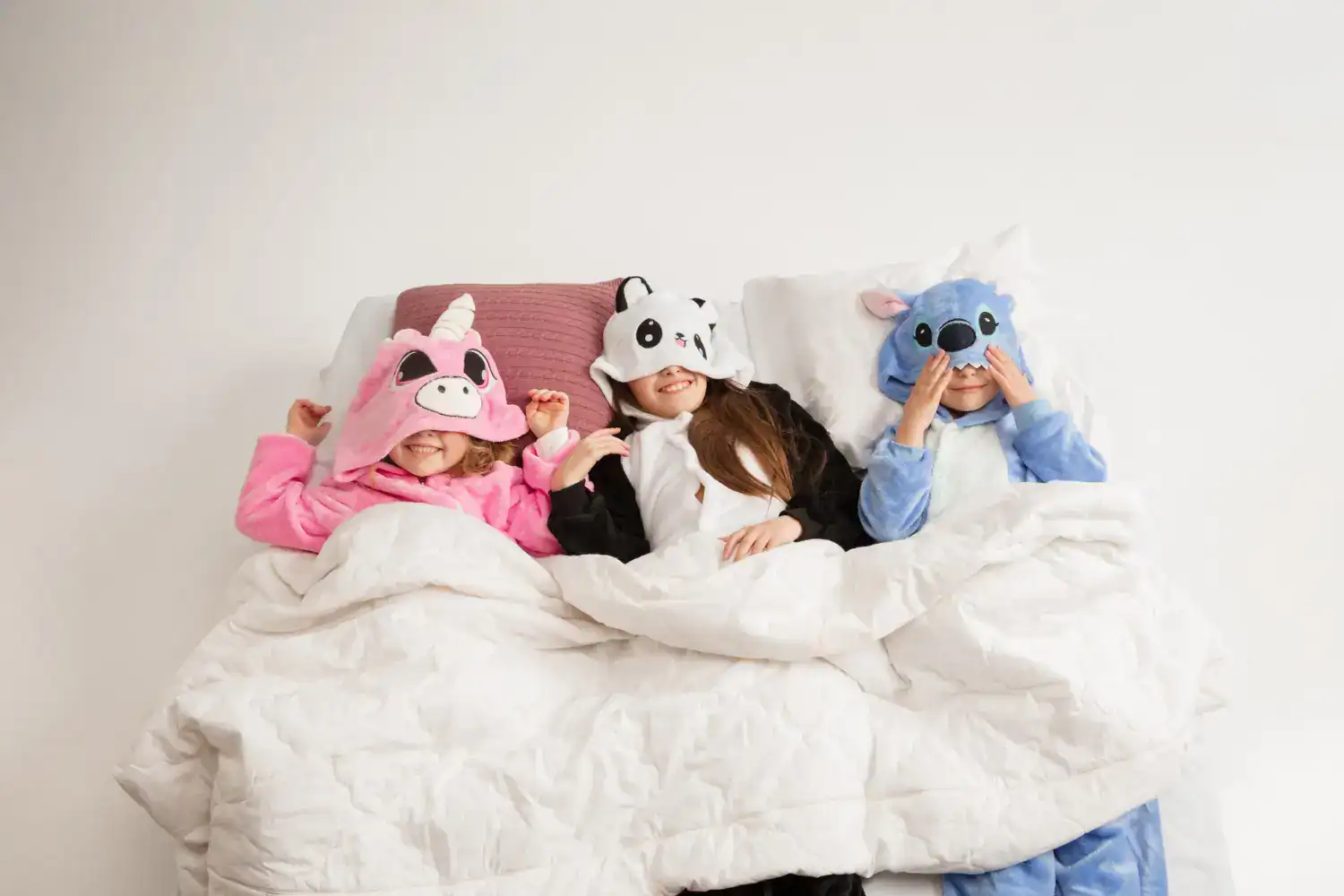Kids in animal-themed sleepover masks having fun in bed.