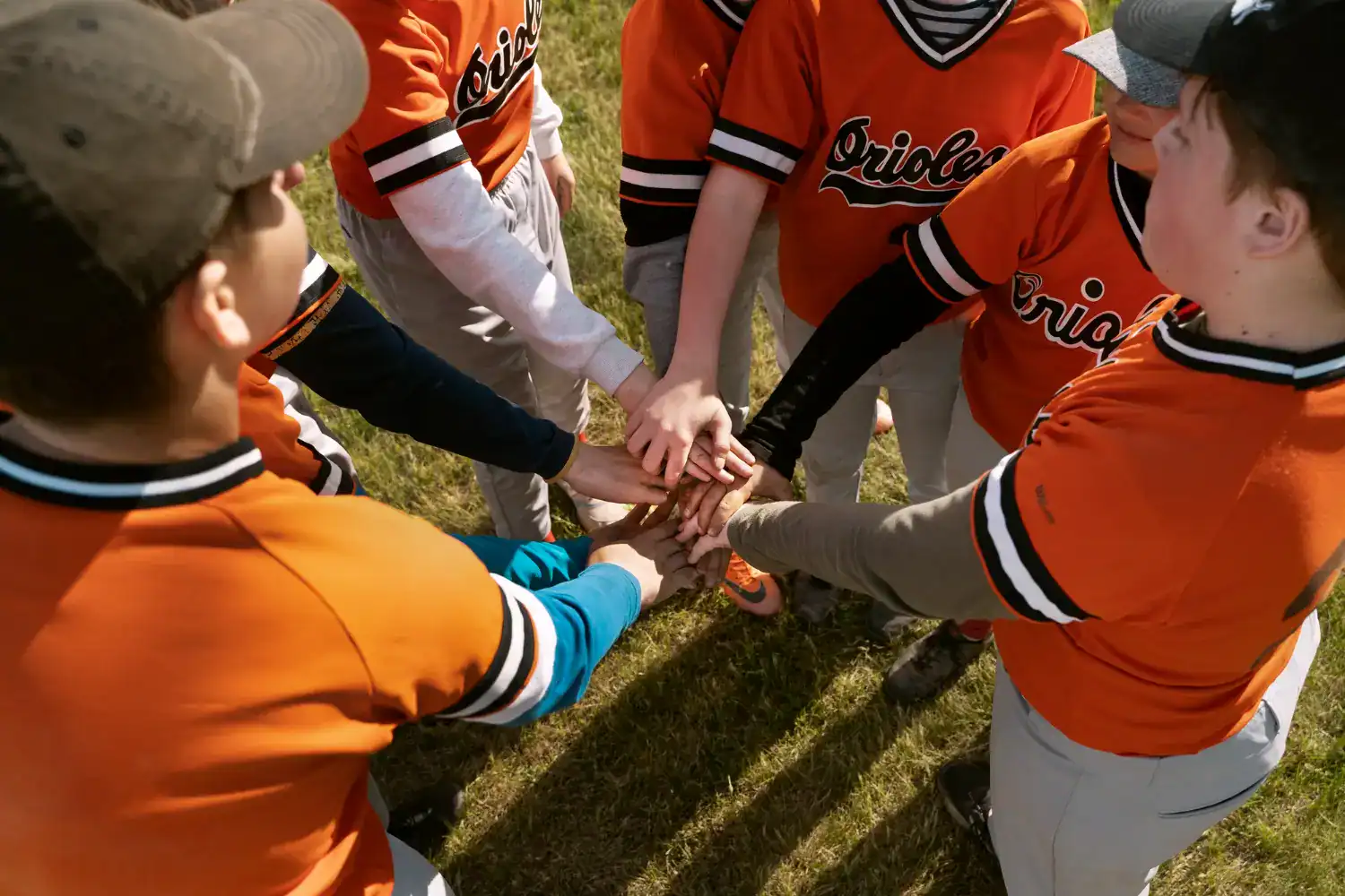 Kids in orange baseball uniforms huddling with hands together on the field.
