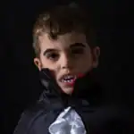 23 Teen Boy Halloween Costumes That Will Turn Heads This Year Young boy in vampire costume with cape and fangs for Halloween.