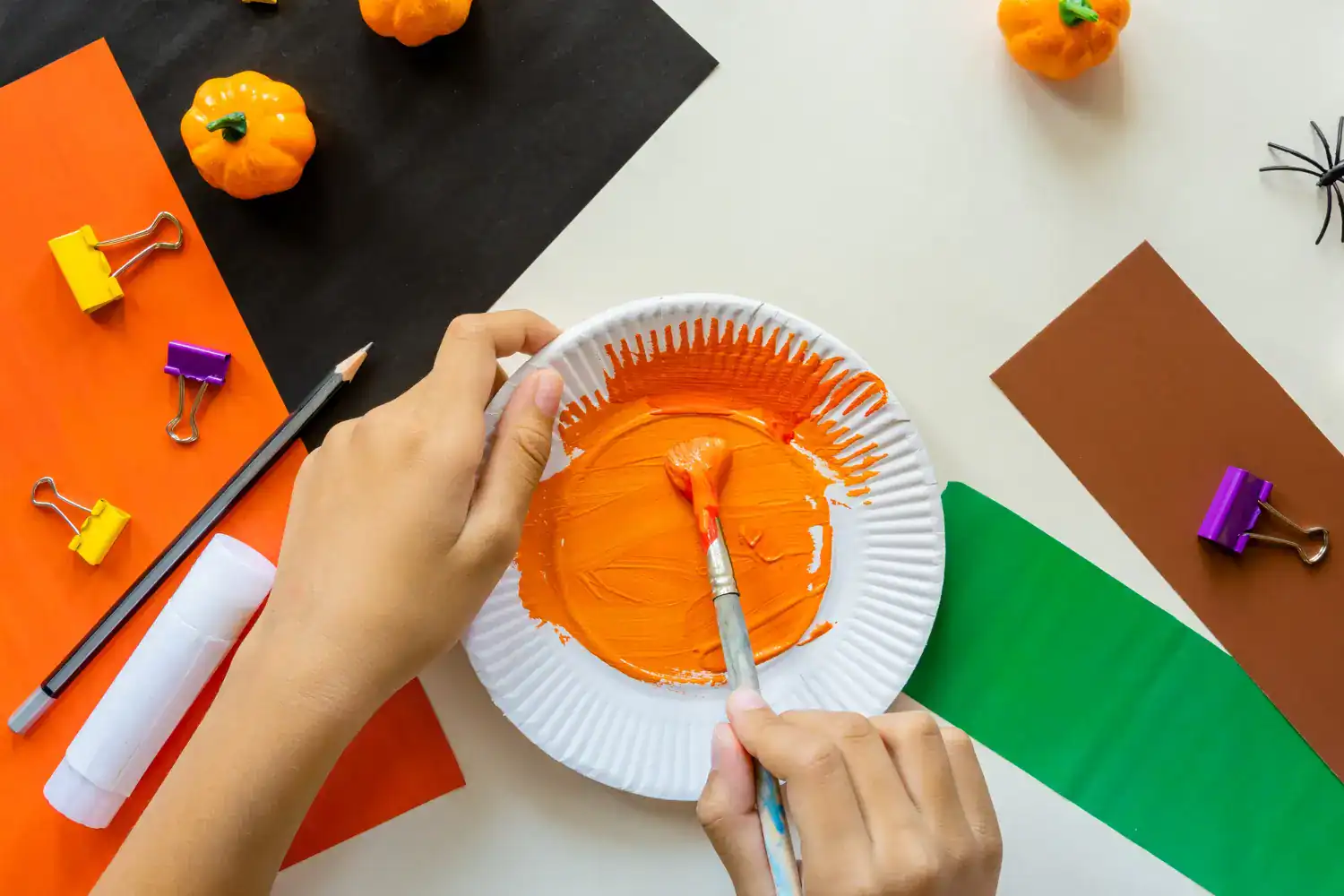 Kids painting pumpkin craft for Thanksgiving with orange paint and paper supplies.