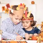 23 Festive Thanksgiving Activities for Kids Kids making Thanksgiving craft with turkey headbands and autumn decorations.