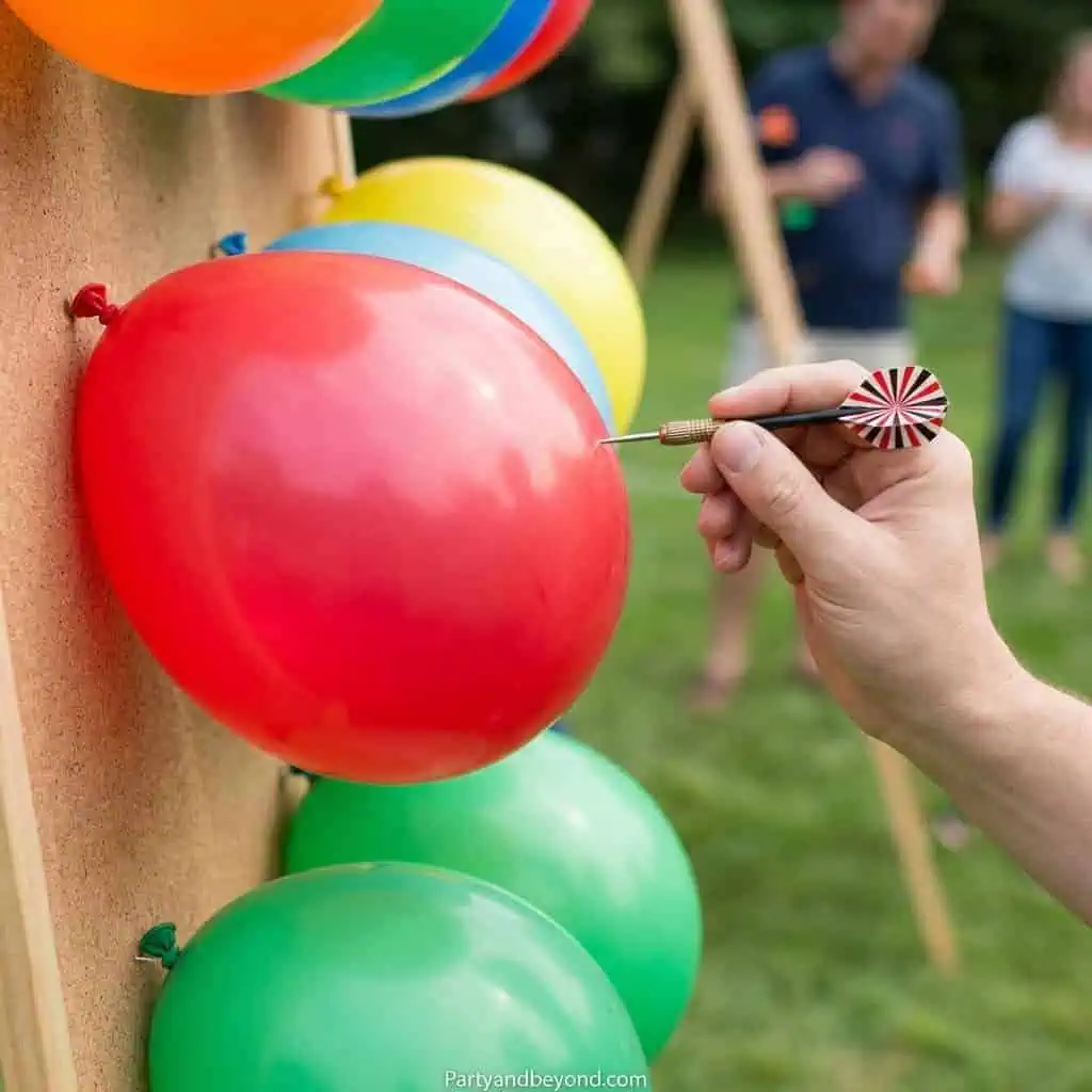 Person popping a red balloon with a dart at a colorful outdoor party game.
