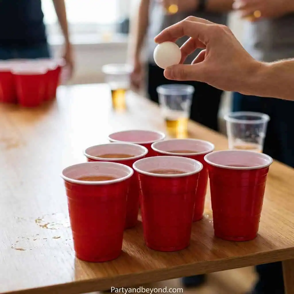 Beer pong game with red cups and a ping pong ball at a party.