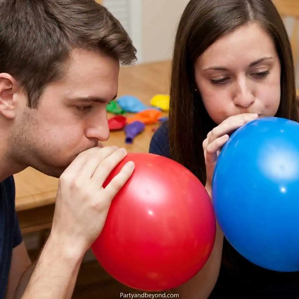 Two people blowing up balloons at a party, fun and laughter.