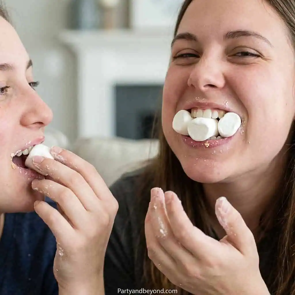 Two women enjoying a fun marshmallow challenge at a party.