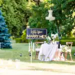 21 Engaging Wedding Lawn Games to Keep the Party Going Romantic outdoor marriage proposal with a "Will You Marry Me?" sign, elegant table, and floral decor.