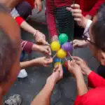 25 Hilarious Minute To Win-It Games Using Household Objects Group of people playing Minute to Win-It game with colorful balls and household objects.