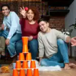 25 New Year’s Eve Games for Family Fun Group of friends playing a fun stacking game with orange cups at home.