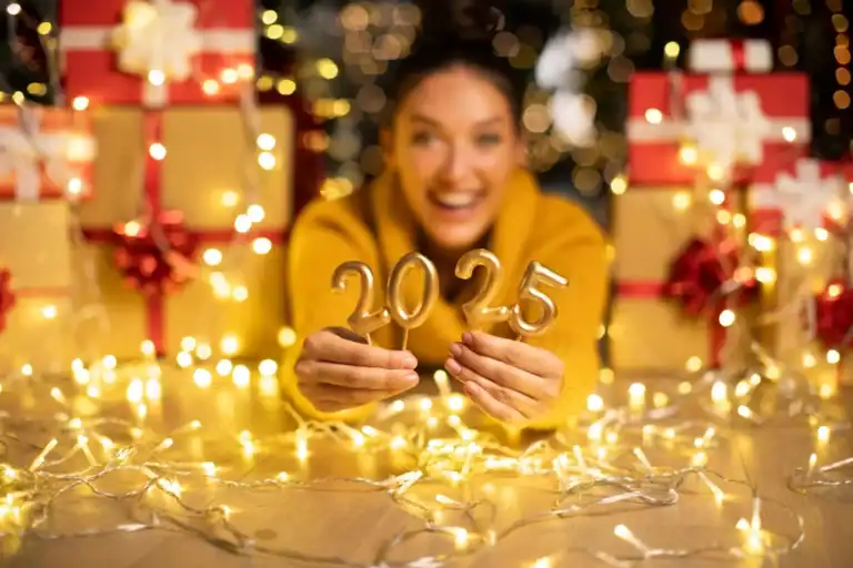 Happy woman holding "2025" candles with festive decorations and gifts in the background.