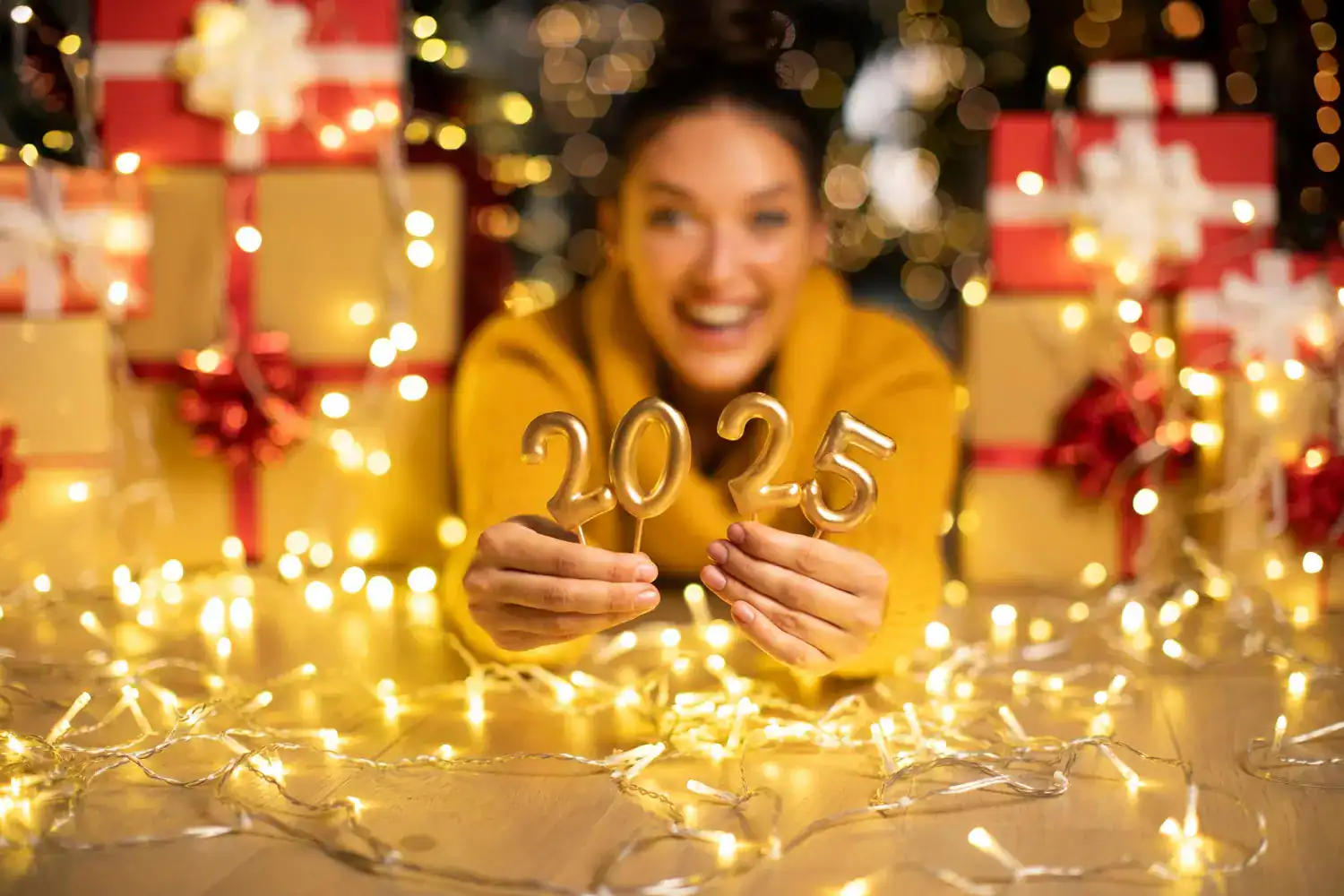 Happy woman holding "2025" candles with festive decorations and gifts in the background.