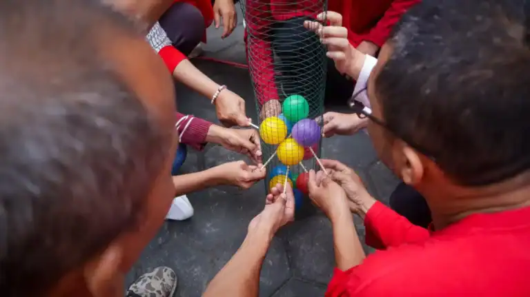 Group of people playing Minute to Win-It game with colorful balls and household objects.