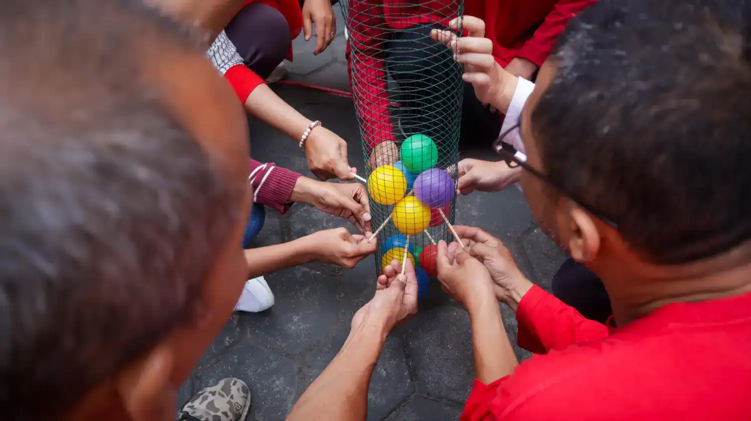 Group of people playing Minute to Win-It game with colorful balls and household objects.