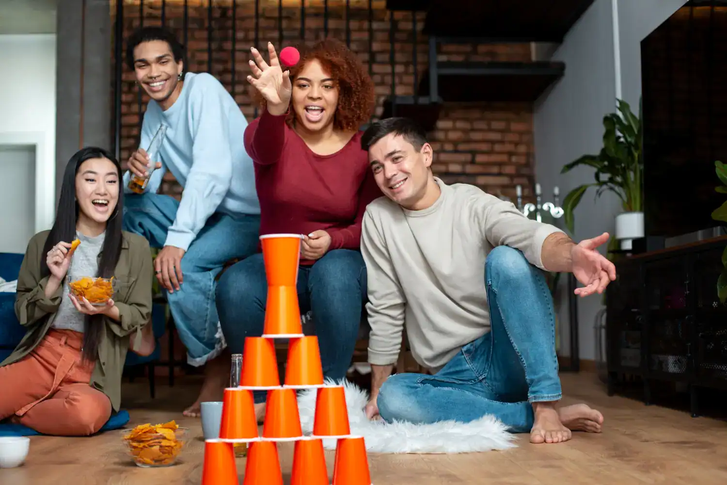 Group of friends playing a fun stacking game with orange cups at home.
