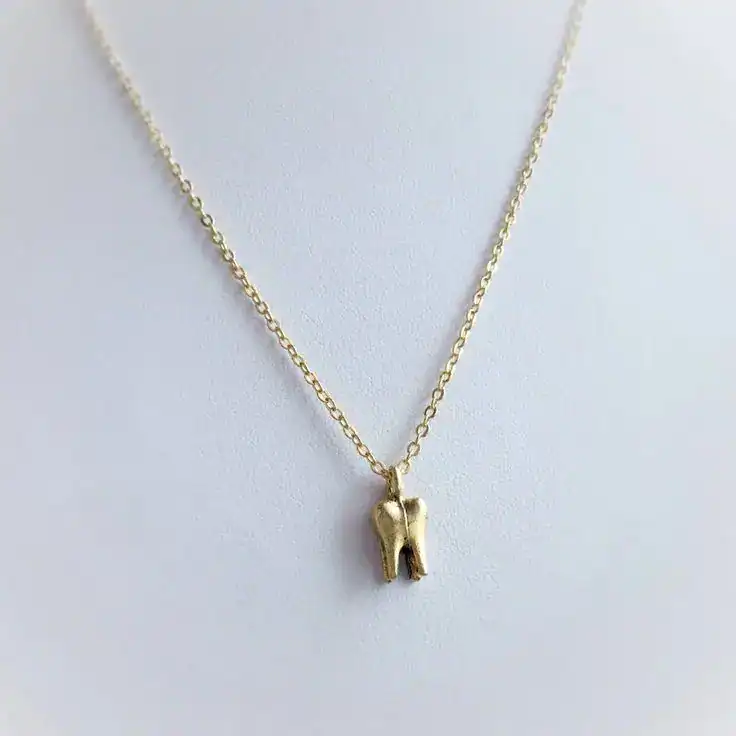 Gold tooth pendant necklace for baby’s first tooth celebration.