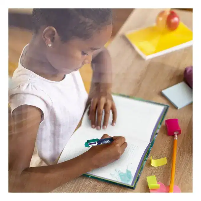 Child writing in a notebook with colorful stationery on a wooden desk.