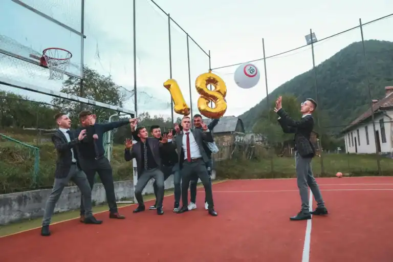 Group of young men celebrating 18th birthday with balloons on outdoor basketball court.