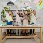 21 Spirit Week Ideas for Work Women celebrating Spirit Week at work with papers flying in an office setting.