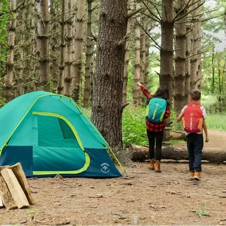 Kids camping in the woods with a tent and backpacks, enjoying outdoor adventure.
