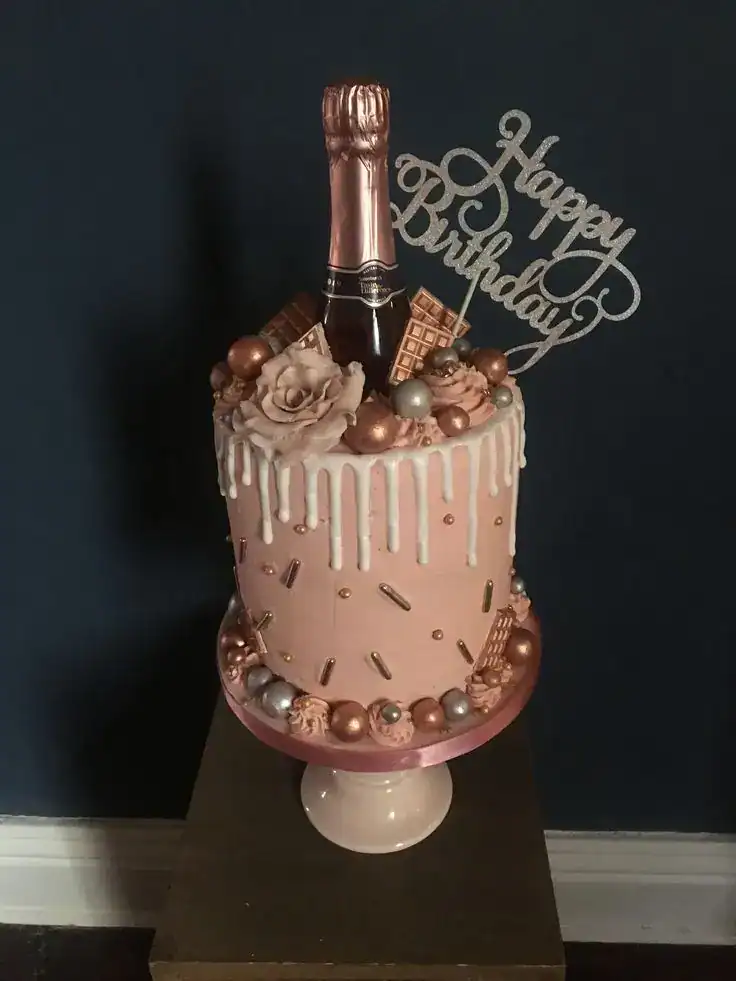 Champagne-infused birthday cake with gold drip, metallic decorations, and a miniature champagne bottle topper for an adult celebration
